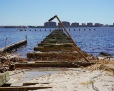 Fishing pier after Hurricane Ian. The City photo looks from shore along the remains of the storm-damaged pier, showing missing decking and exposed piles that led to the full-rebuild plan.
